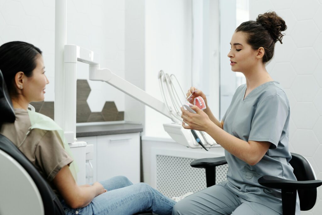 A female dentist in scrubs is explaining a dental model to a patient in a modern dental clinic.