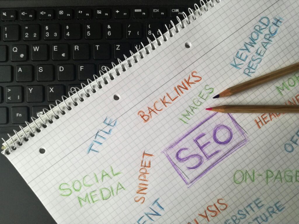 A notebook on a laptop keyboard with handwritten SEO terms including "SEO," "Keyword Research," "Backlinks," "Social Media," and "Title."
